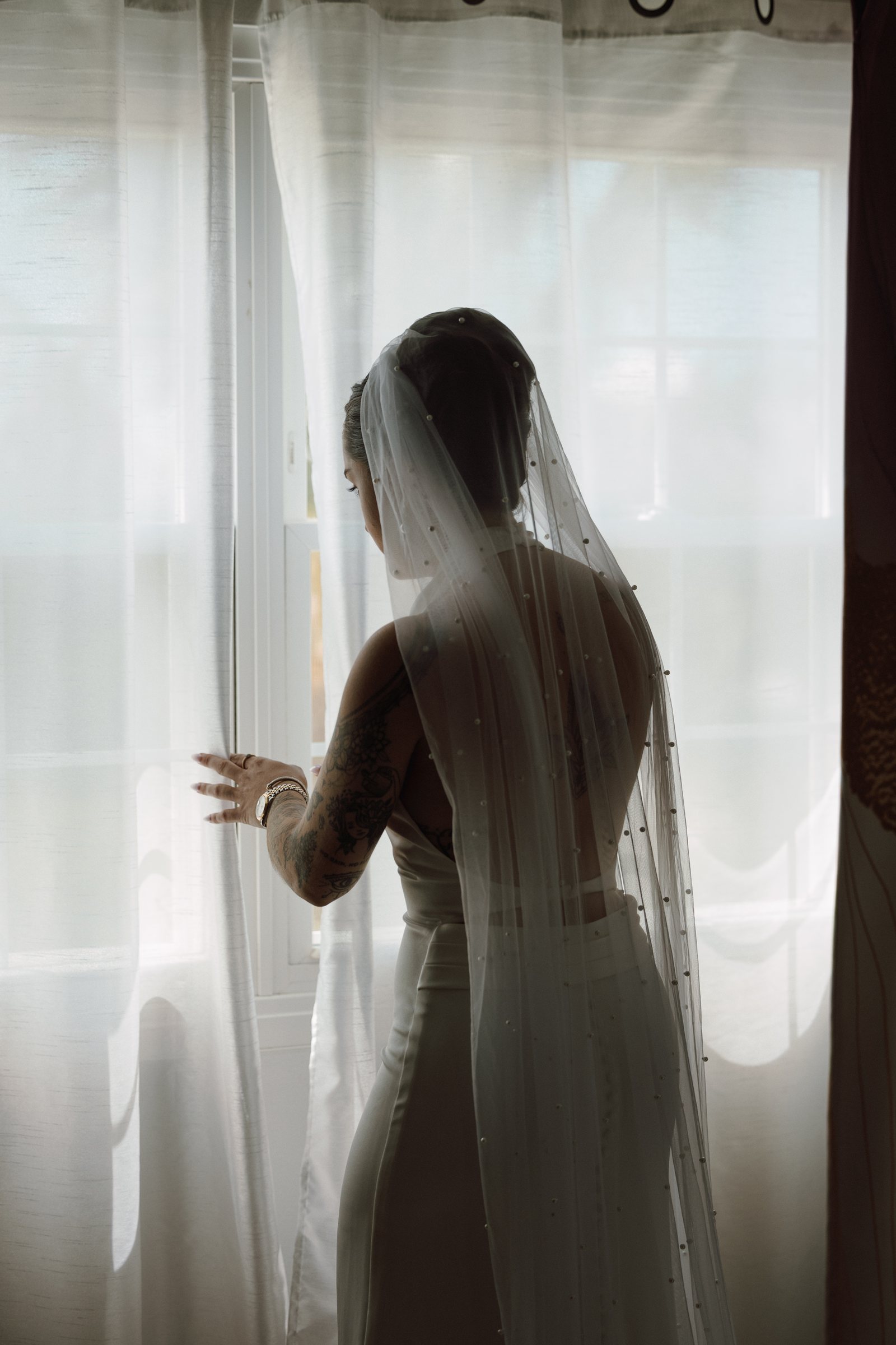 Bride standing at the window in her veil during getting ready
