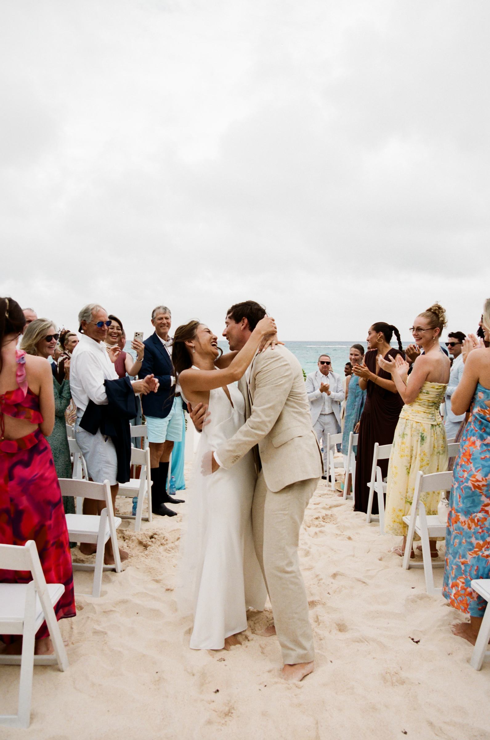 Bride and groom walking the recessional across the sand as guests cheer