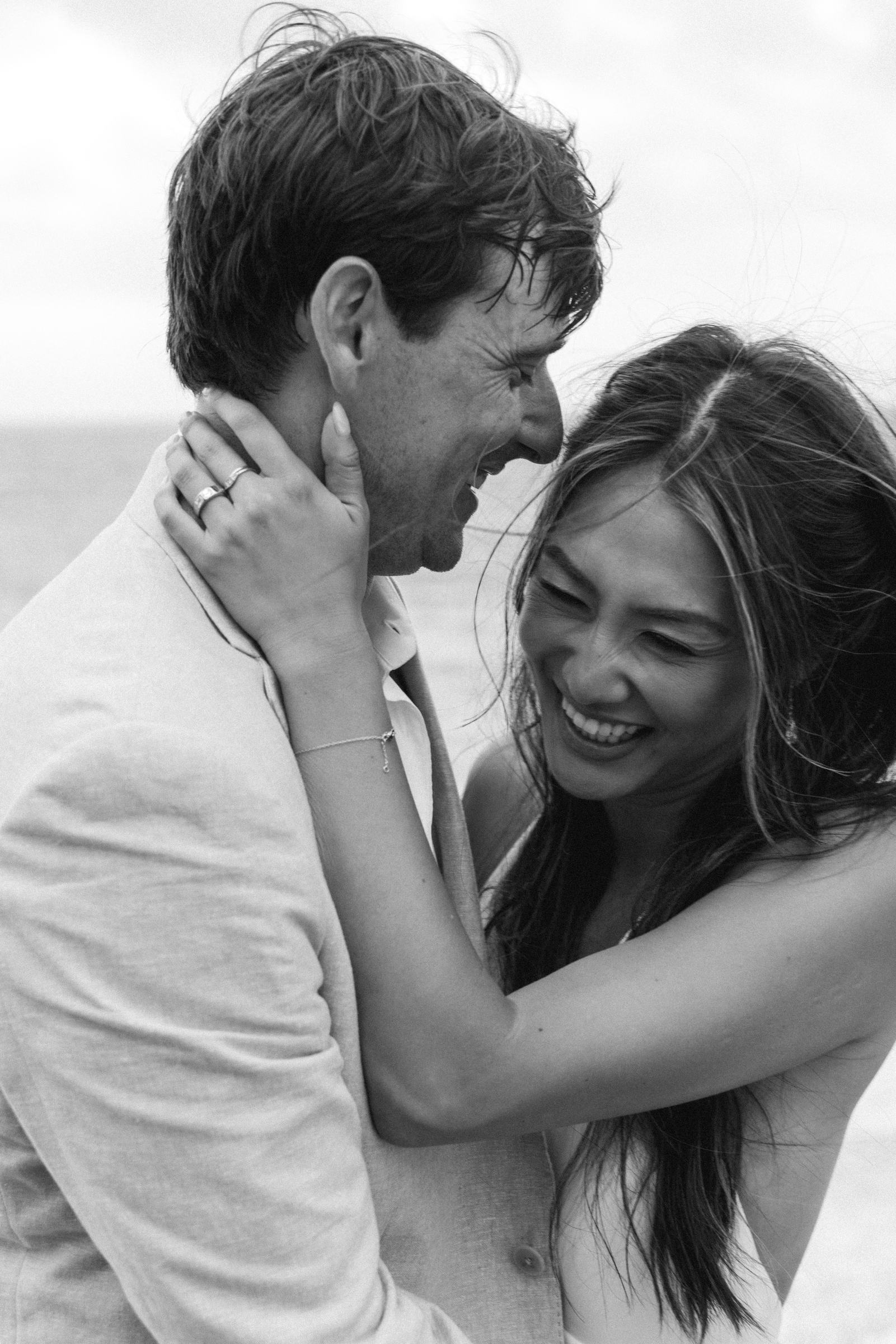 Black and white photograph of the bride laughing with her arms around the groom