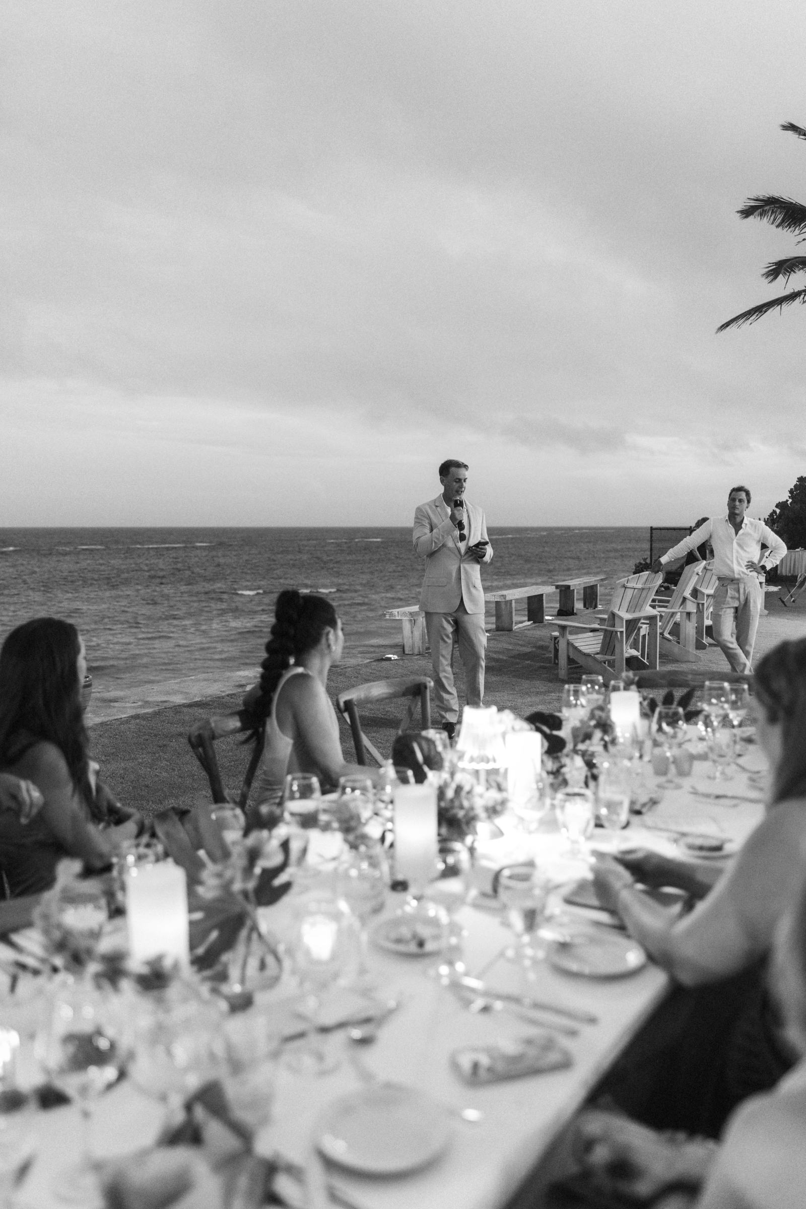 Black and white photograph of the long dinner table beside the water at dusk