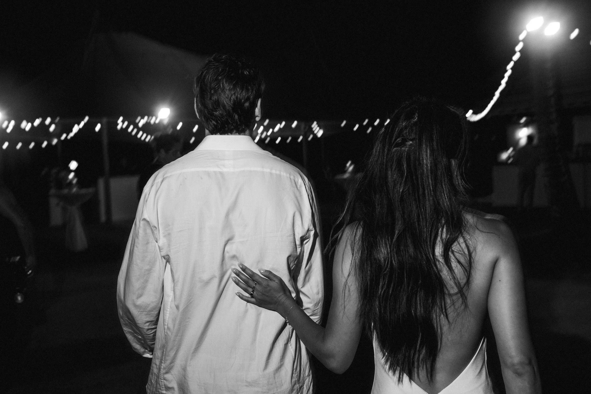 Black and white photograph of the couple walking away together under the string lights