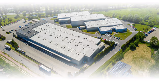 Aerial view of a large industrial facility with multiple warehouse buildings surrounded by parking lots and greenery.