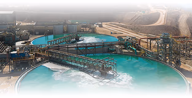 Aerial view of a large mining facility with metal processing tanks filled with turquoise water and industrial equipment.