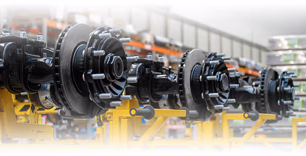 Row of automotive wheel hub assemblies mounted on yellow stands in a factory or workshop setting.