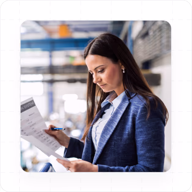 Professional woman in a blue blazer reviewing a printed document in an industrial or office setting.