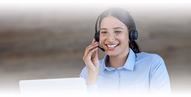 Smiling woman wearing a headset and blue shirt, working at a laptop, representing customer support.