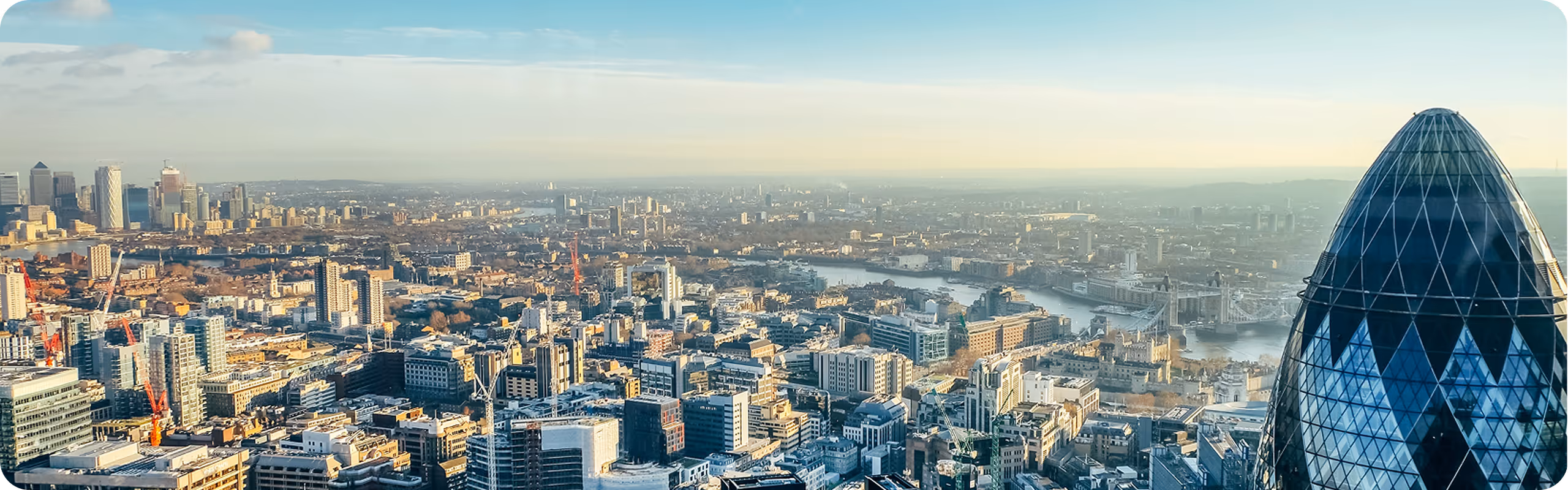 Panoramic view of London skyline featuring the Gherkin skyscraper and the River Thames under a clear sky.