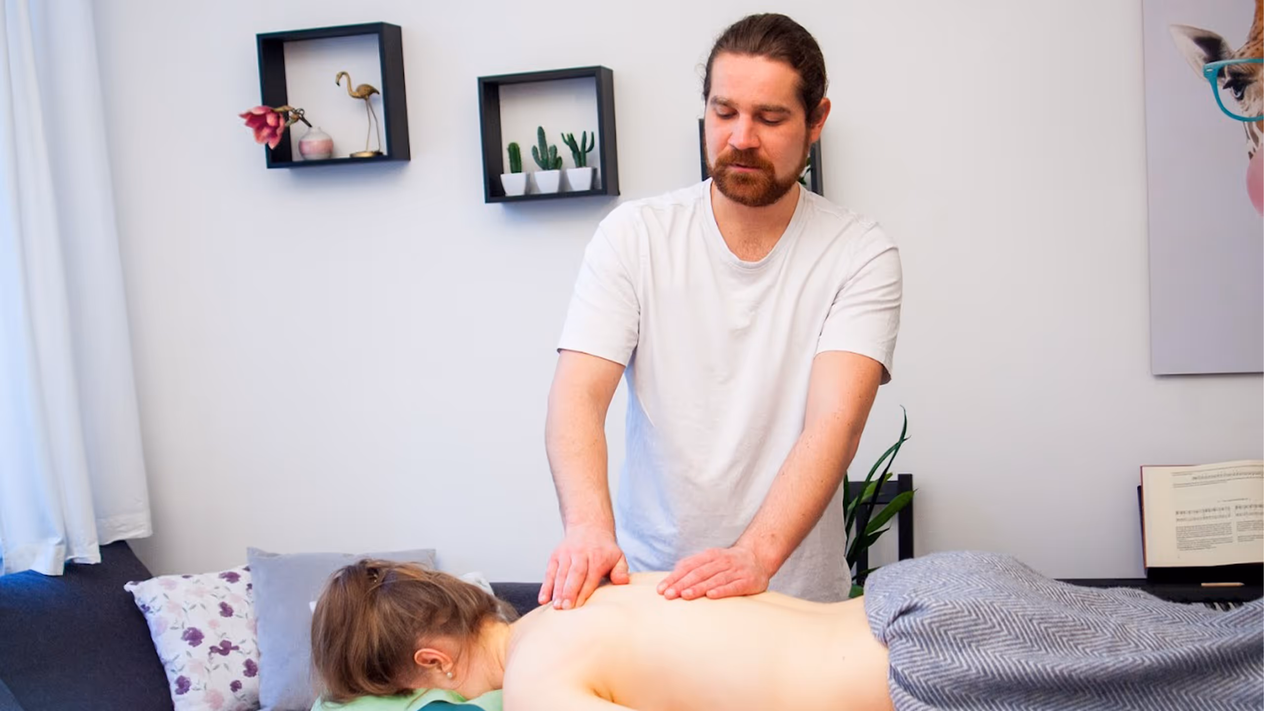 Der Heilmasseur Markus Anderle gibt einer Frau eine Rückenmassage auf einer Massageliege mit grauer Decke