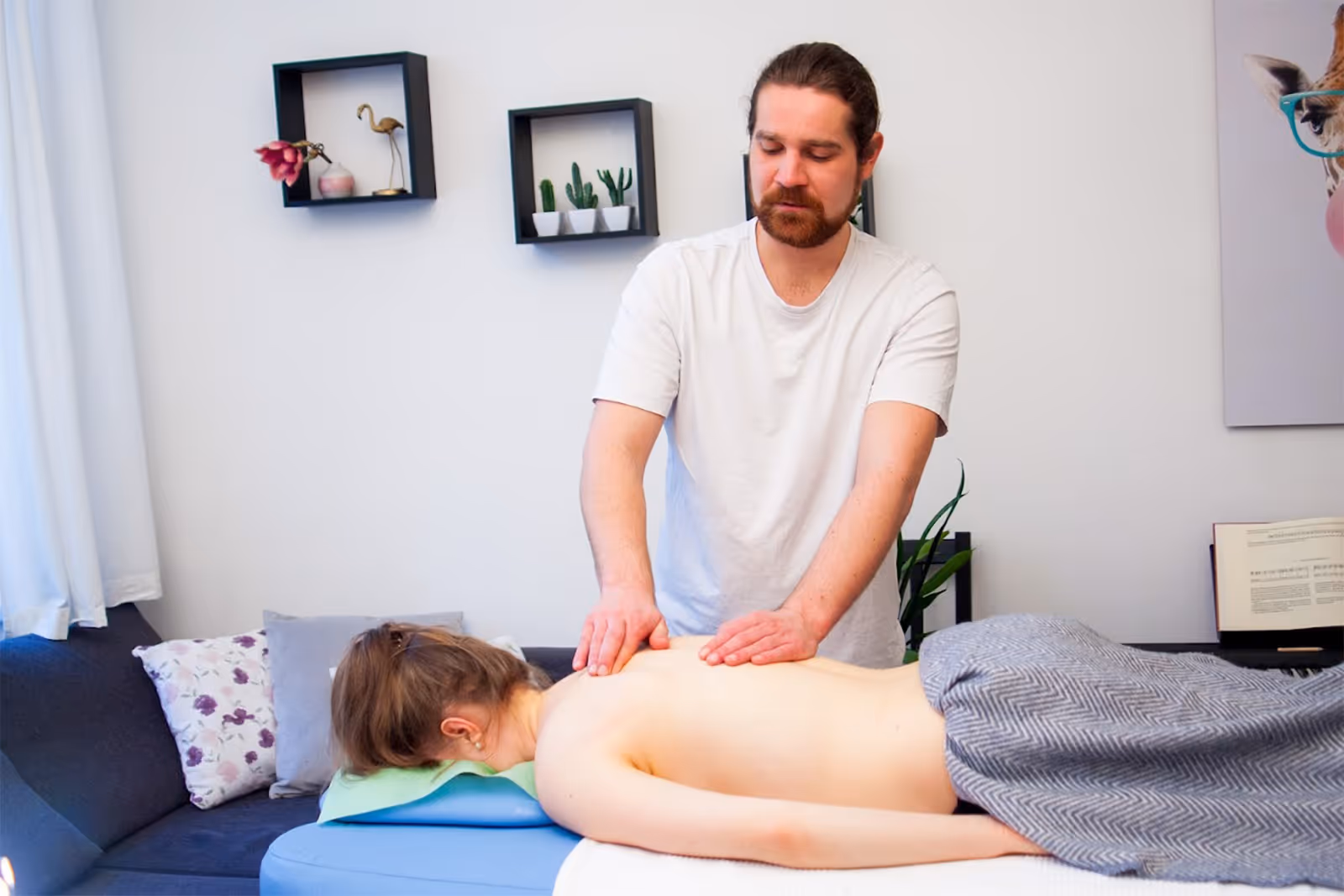 Der Heilmasseur Markus Anderle gibt einer Frau eine Rückenmassage auf einer Massageliege mit grauer Decke