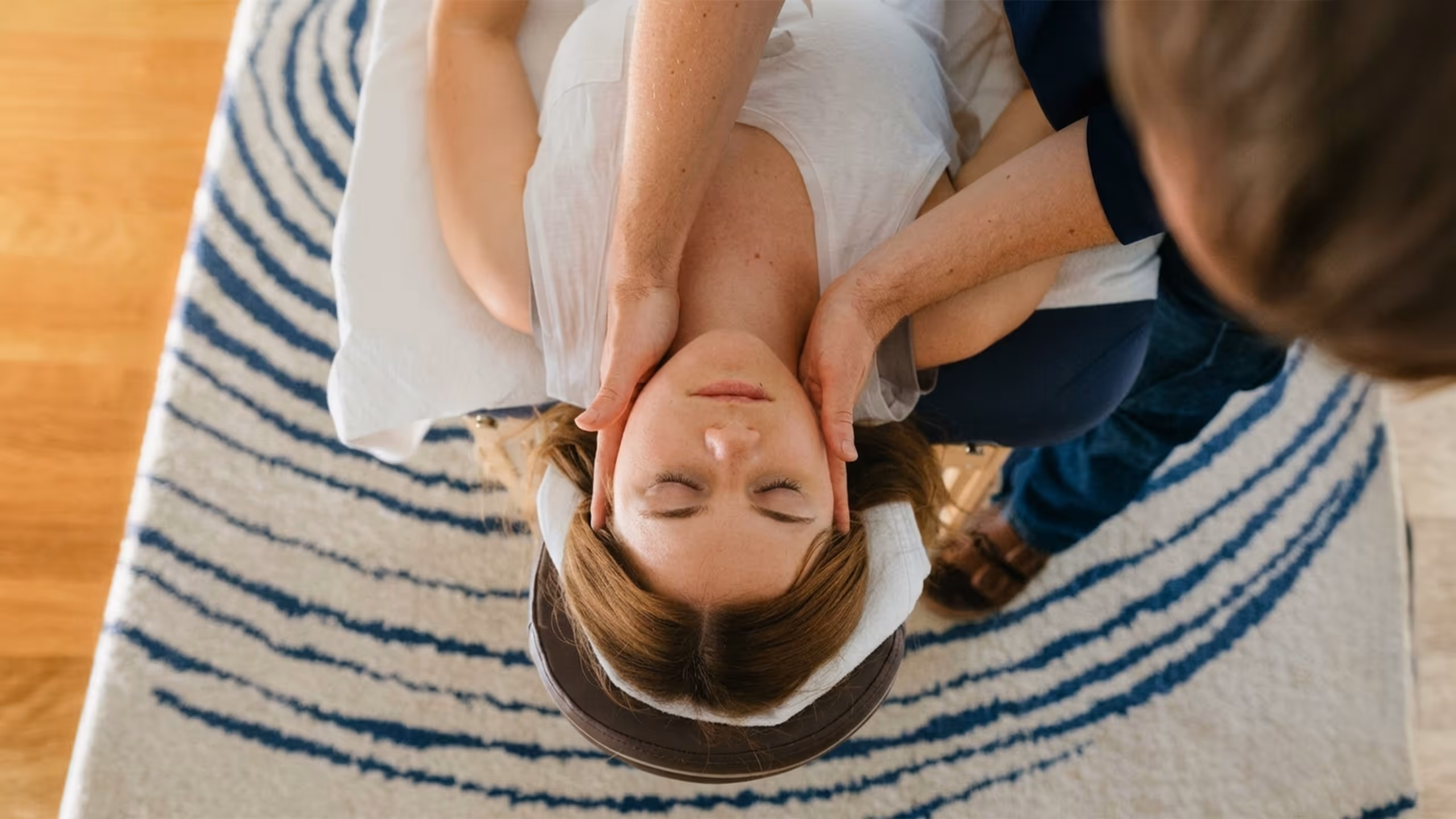 Frau liegt mit geschlossenen Augen auf der Massageliege und erhält eine Kopfmassage