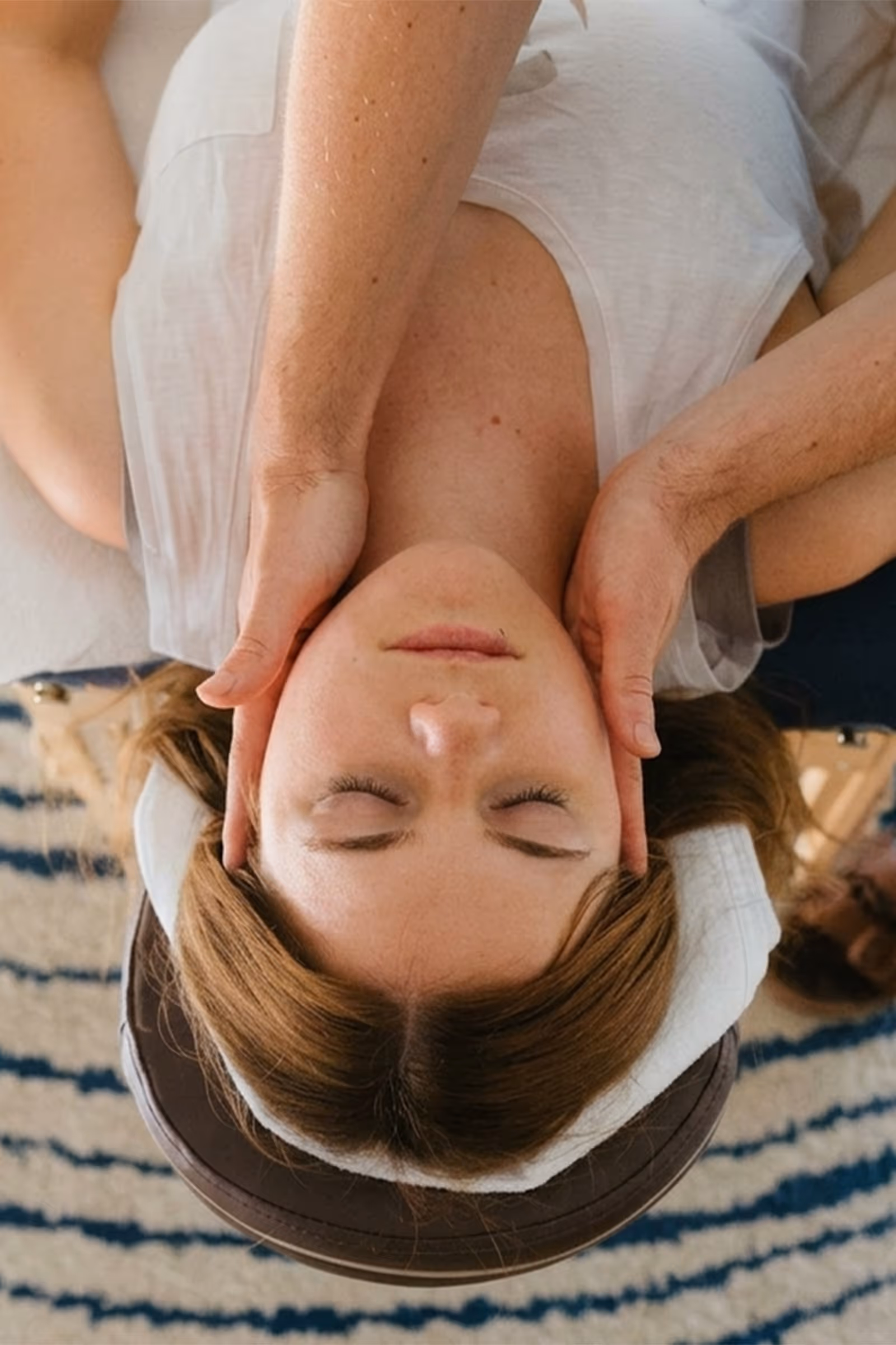 Frau liegt mit geschlossenen Augen auf der Massageliege und erhält eine Kopfmassage
