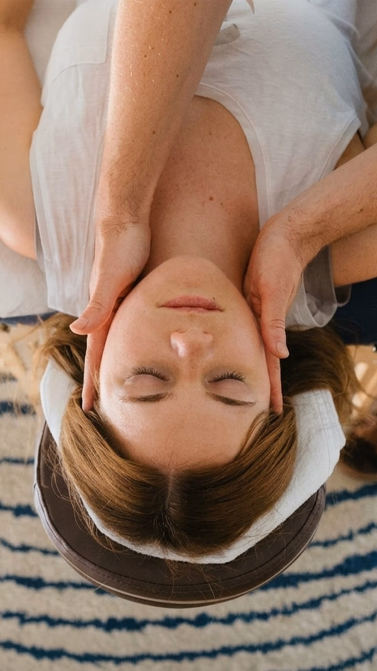 Frau liegt mit geschlossenen Augen auf der Massageliege und erhält eine Kopfmassage