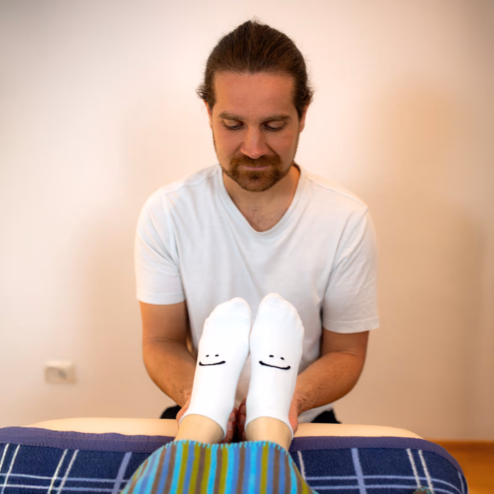 Mann hält Füße mit weißen Socken mit Smileys während einer Massagesession