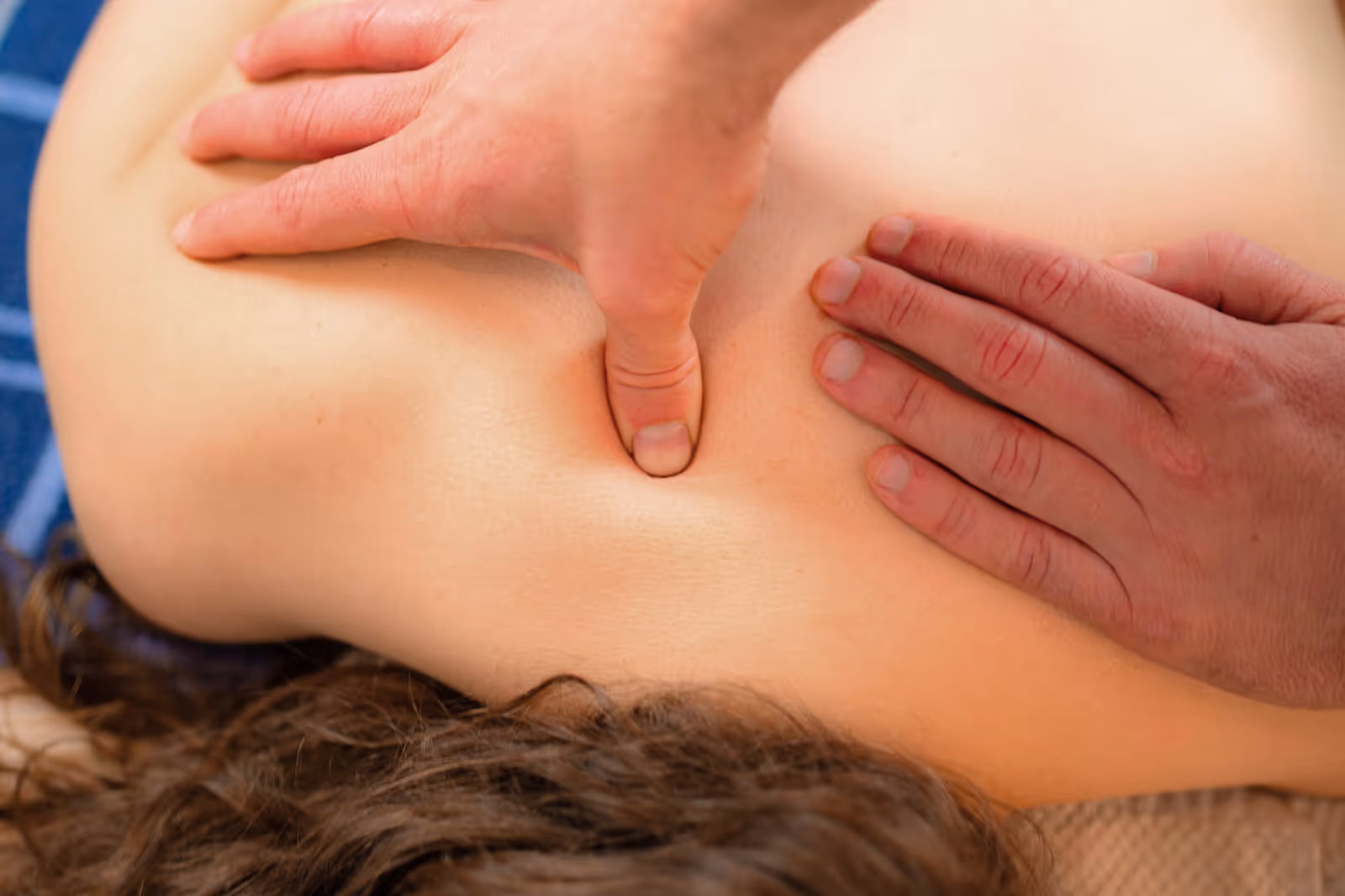 Heilmasseur übt sanft Druck zwischen den Schulterblättern einer Patientin aus