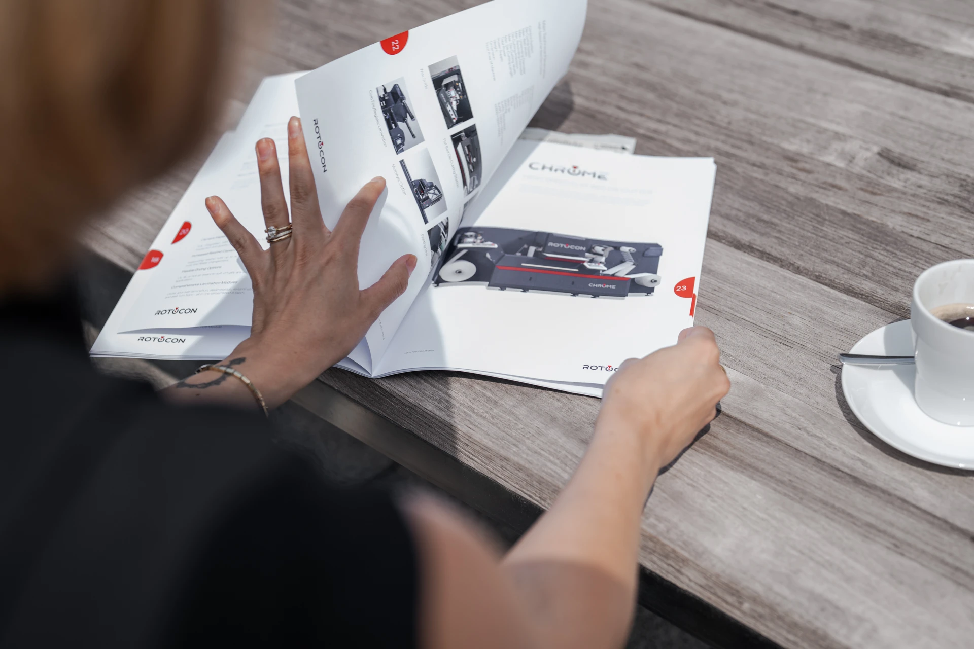 Person flipping through a Rotocon product catalog on a wooden table next to a cup of coffee.