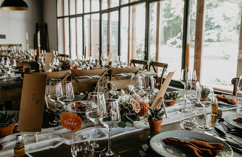 Grande table de mariage décorée avec des bougies et des compositions florales dans la salle de réception de La Ferme Marie Hélène.