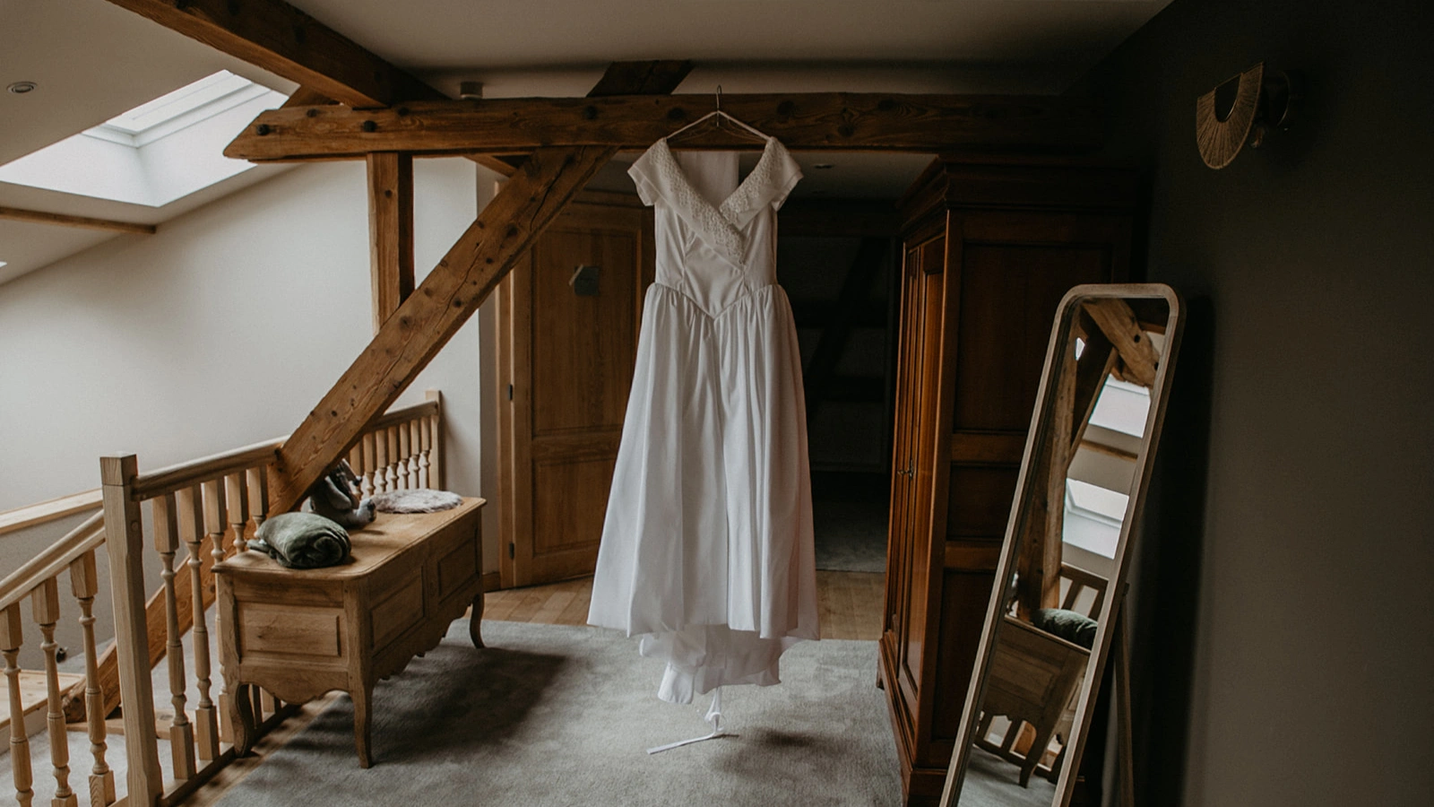 Robe de mariée suspendue dans une chambre à La Ferme Marie Hélène, entourée de poutres en bois et d’un mobilier élégant.