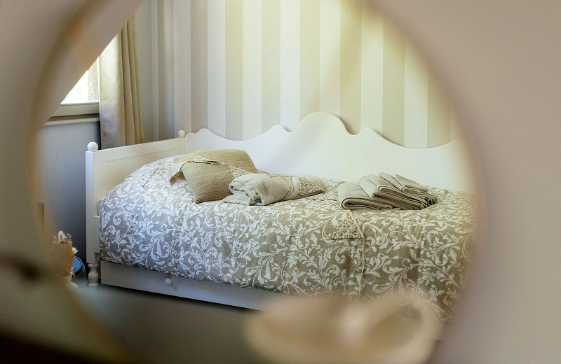 Lit simple élégant de la ferme Marie Hélène, aux motifs fleuris, photographié à travers un miroir avec serviettes pliées et coussins assortis.