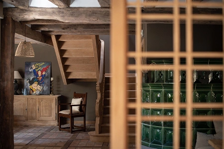 Intérieur rustique avec escalier en bois et poêle en céramique verte, capturant l’authenticité et le confort de La Ferme Marie Hélène.