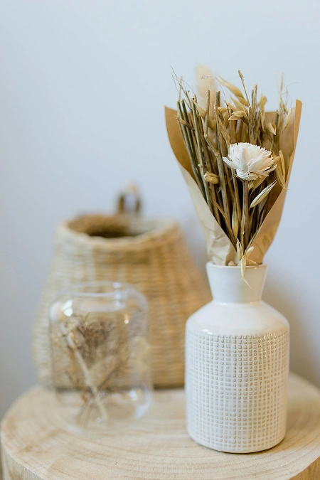 Délicat bouquet de fleurs séchées dans un vase en céramique blanche, ajoutant une touche bohème à la décoration de La Ferme Marie Hélène.