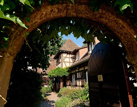 Jolie entrée encadrée par une arche en pierre et végétation luxuriante, accueillant les visiteurs dans l’atmosphère pittoresque de La Ferme Marie Hélène.