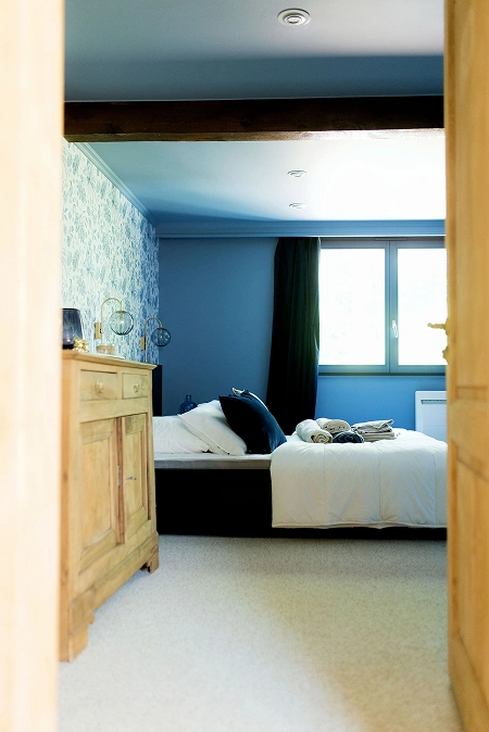 Chambre élégante avec mur bleu et mobilier en bois, offrant une atmosphère relaxante à La Ferme Marie Hélène.