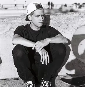 Portrait noir et blanc d'Henri Galine habillé en noir avec une casquette accroupi. Photo de Caroline Vincent.