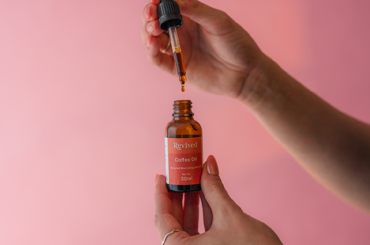 Opening skincare serum glass bottle with orange label saying 'Revived coffee oil'