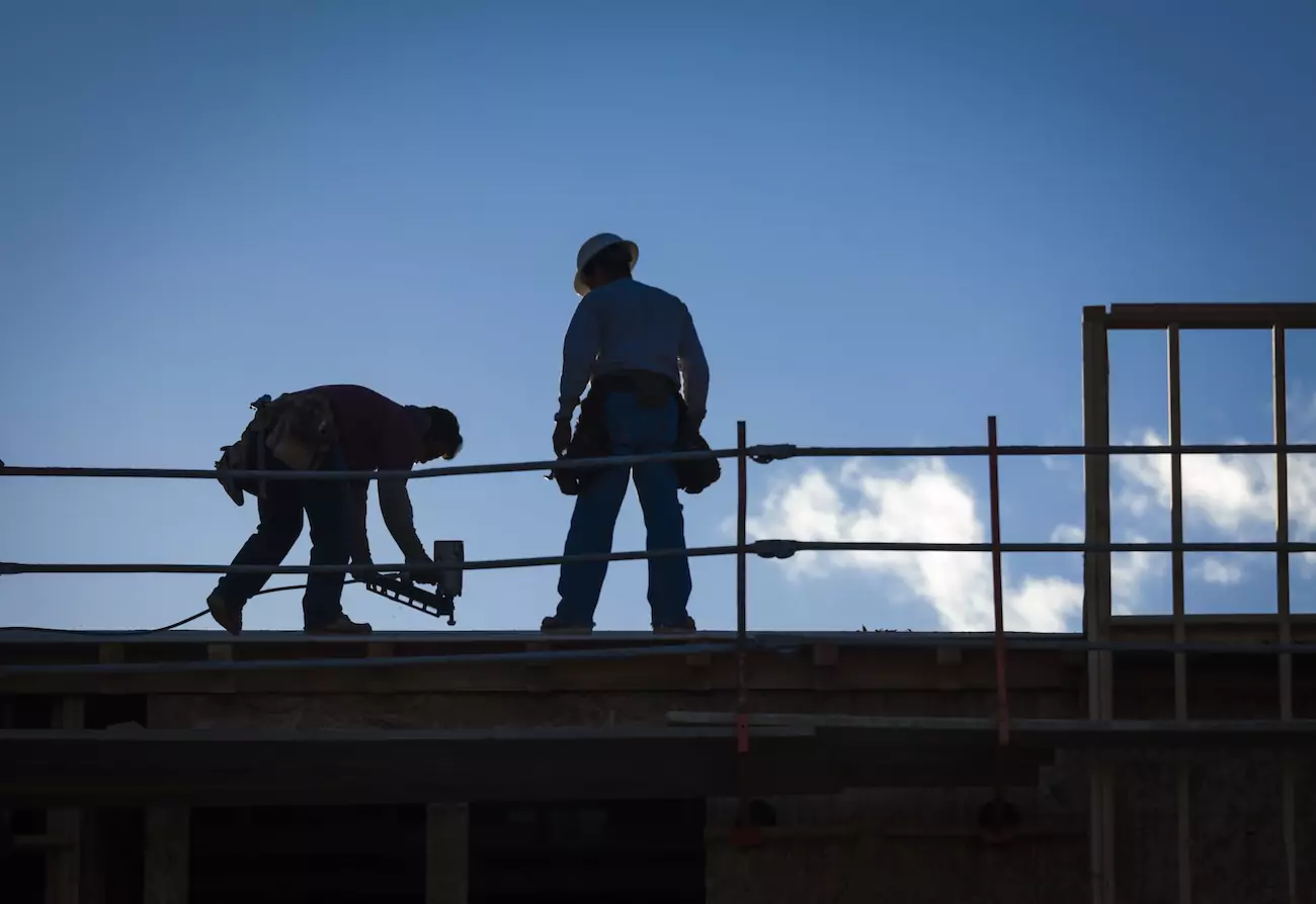 Two roofers repairing a house's roof. 