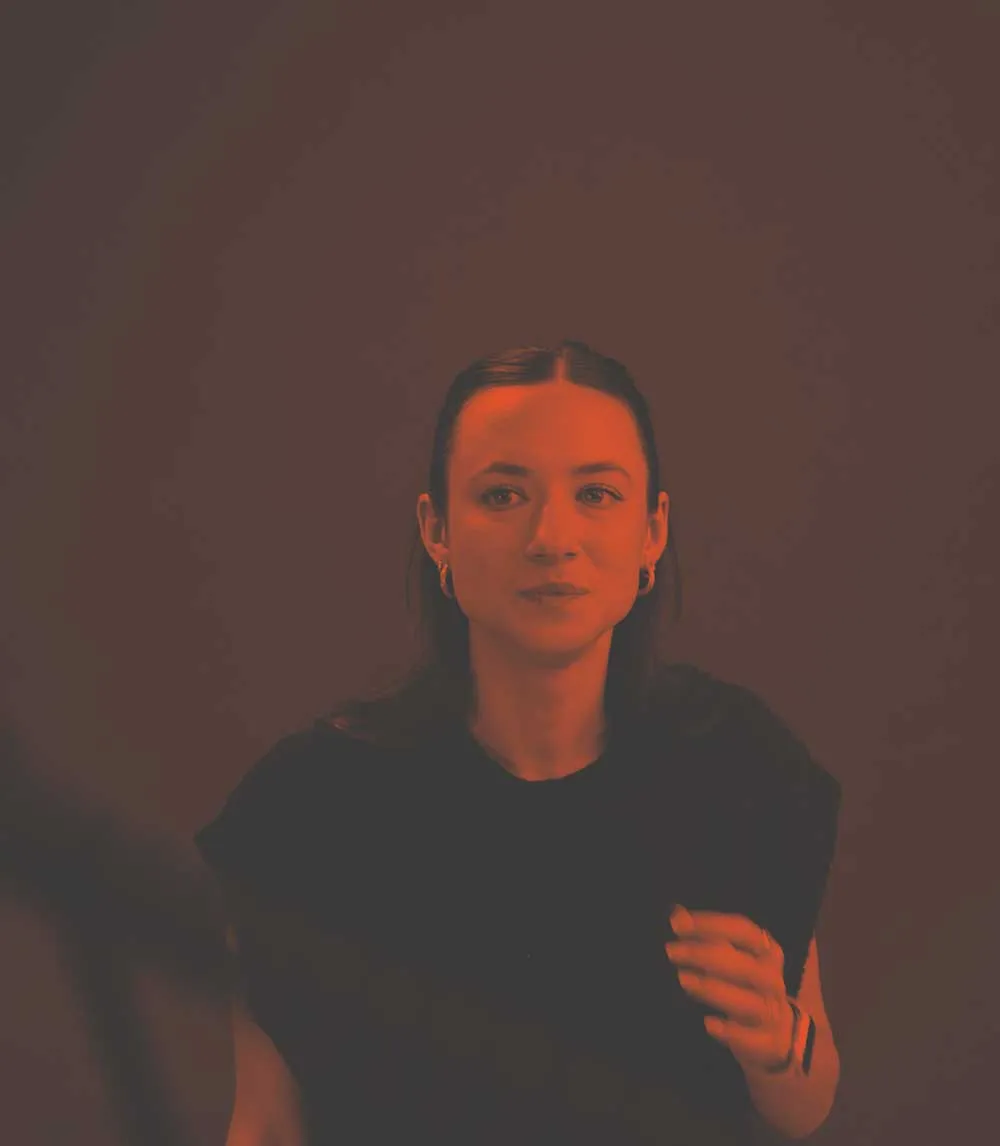 Karina - Kitto Accounts Lead sat in a photography studio staring at the camera. The background is grey with a vignette.