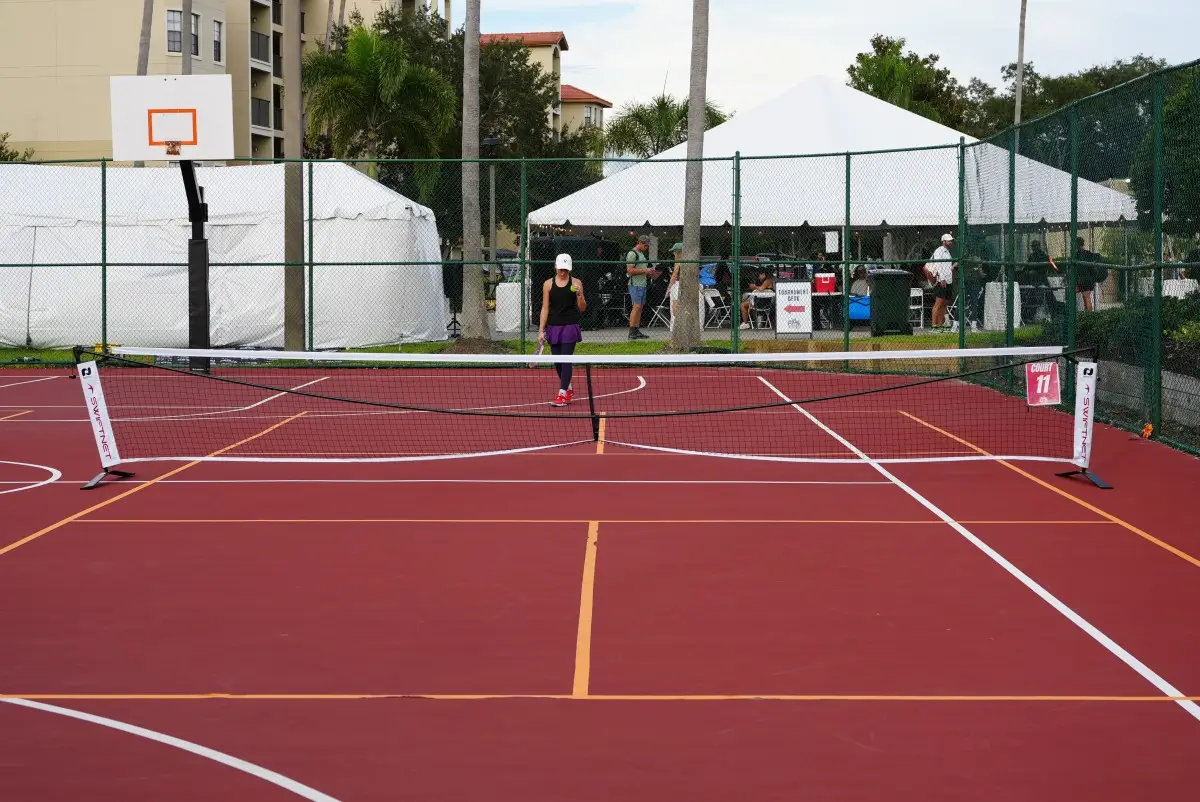 A temporary pickleball setup on a red basketball court with orange tape lines and a flimsy portable net sagging in the middle.