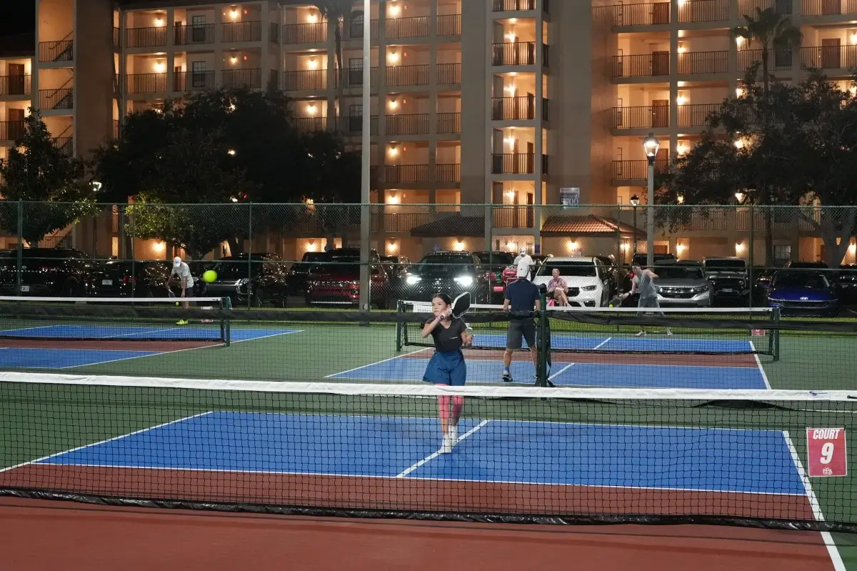 Pickleball players competing at night under poor lighting, with condo lights and car headlights shining directly onto the court.