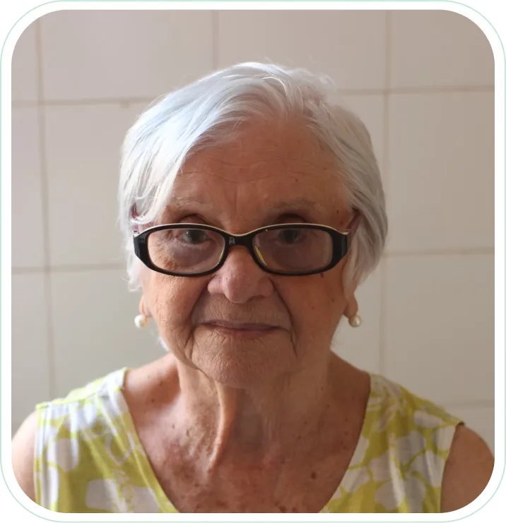 An older woman wearing glasses in front of a tiled wall.