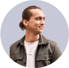 Young man with a bun hairstyle, wearing a jacket and smiling while looking to the side.