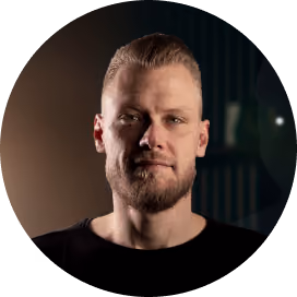 Man with short blond hair and beard wearing a black shirt in a dark setting.