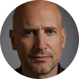 Portrait of a middle-aged bald man with a slight smile against a dark background.