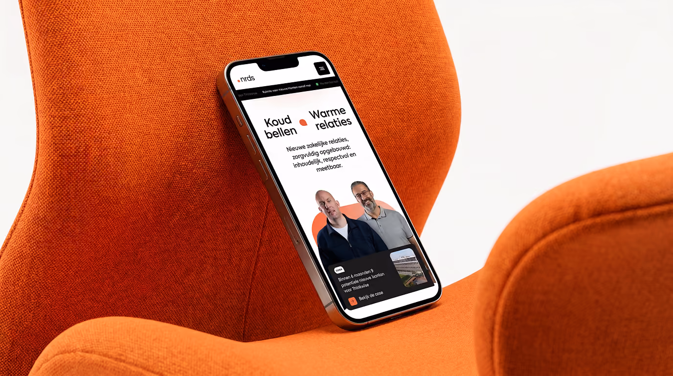 Smartphone resting on an orange fabric chair displaying a website with two men and Dutch text.