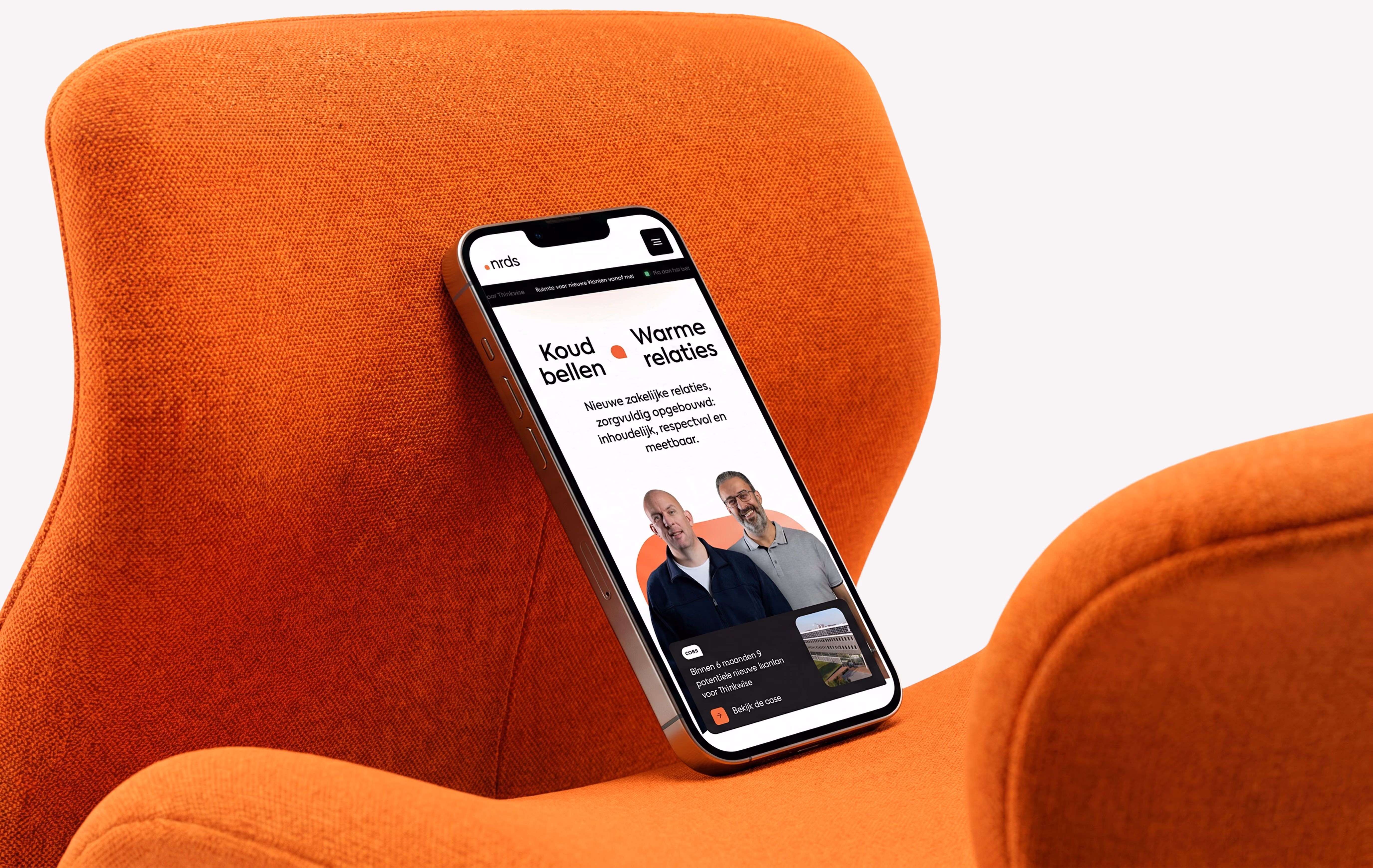Smartphone resting on an orange chair showing a website with two men and Dutch text about business relations.