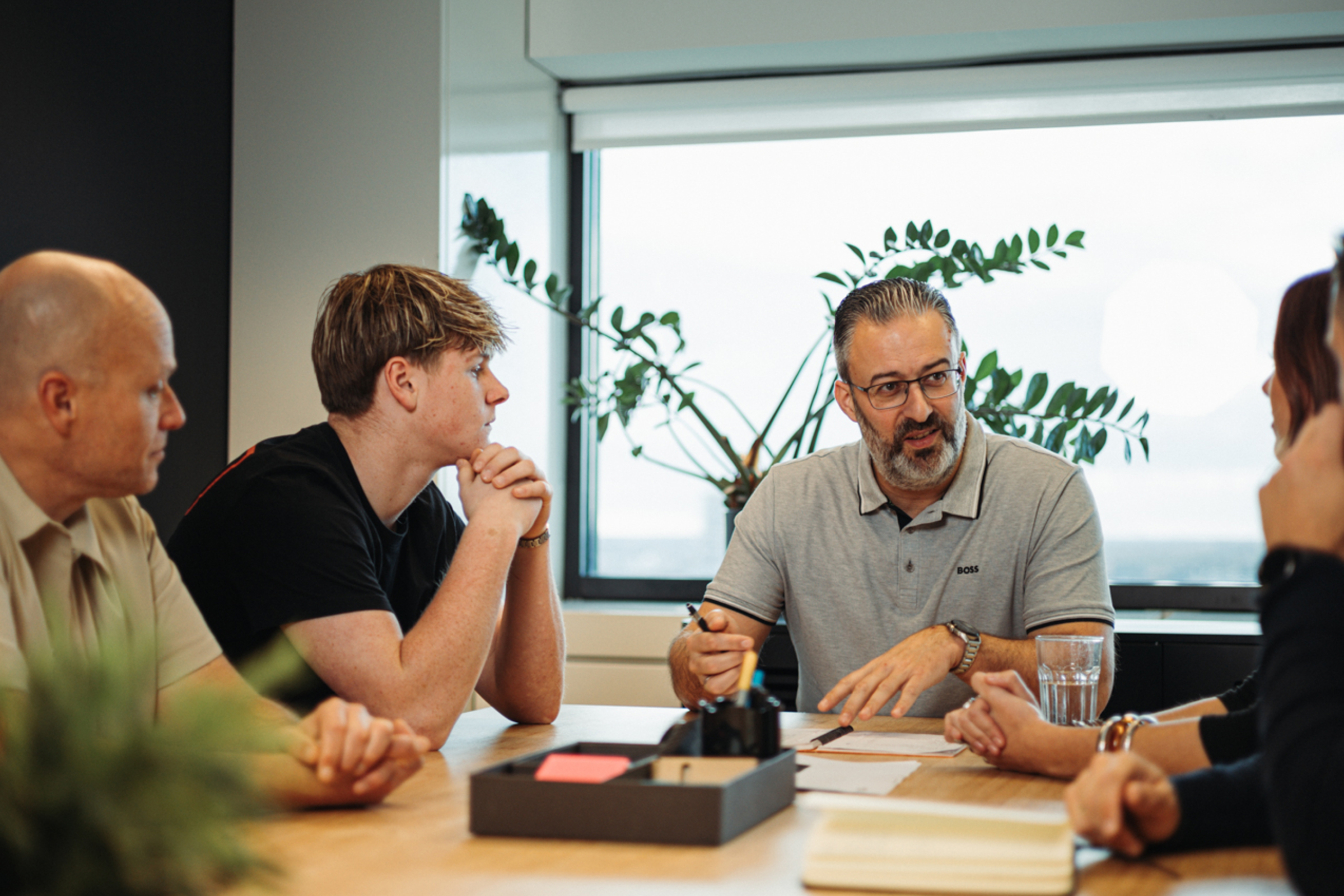 A man in glasses leads a meeting with three attentive colleagues around a conference table.