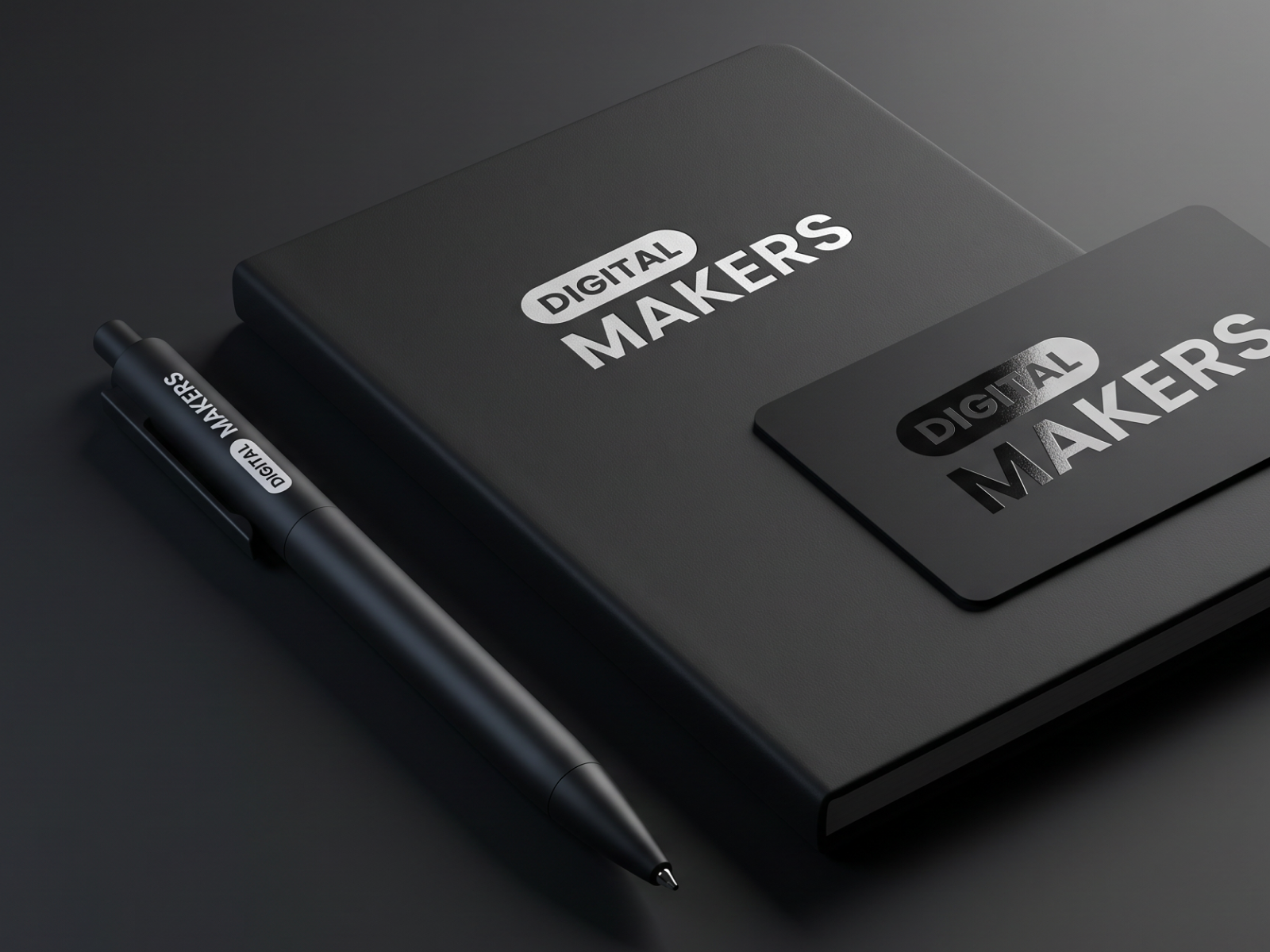 Digitalmakers brand identity on a black notebook, business card and pen