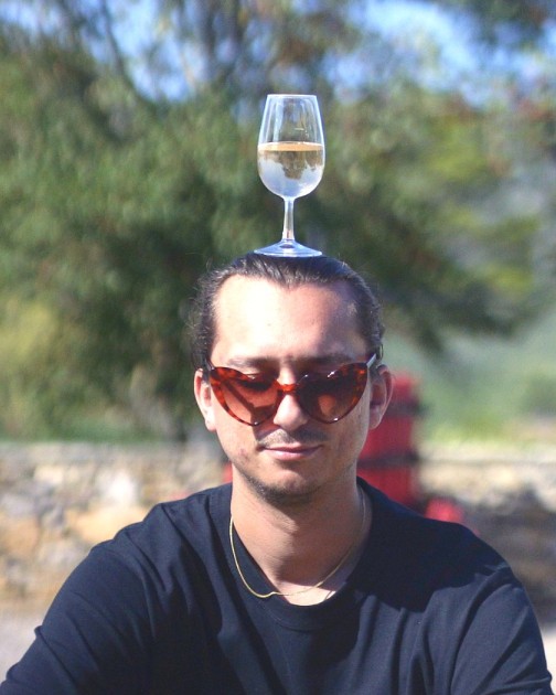 One of the founders in heart-shaped sunglasses, balancing a glass of rosé on his head