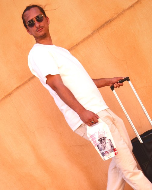 A man with a rolling suitcase carries the Bowi pouch past an orange wall