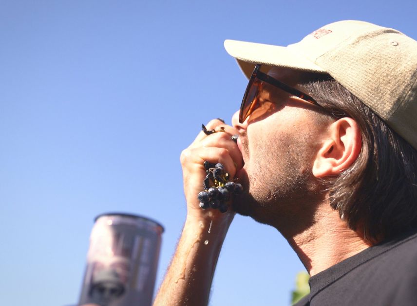 A man in a cap eats grapes next to a Bowi can