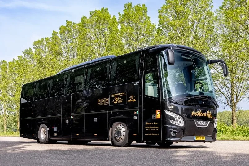 A black VIP coach in front of a row of trees