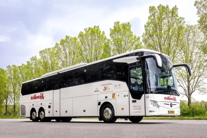 A white touring coach of Royal Oostenrijk Group in front of a row of trees