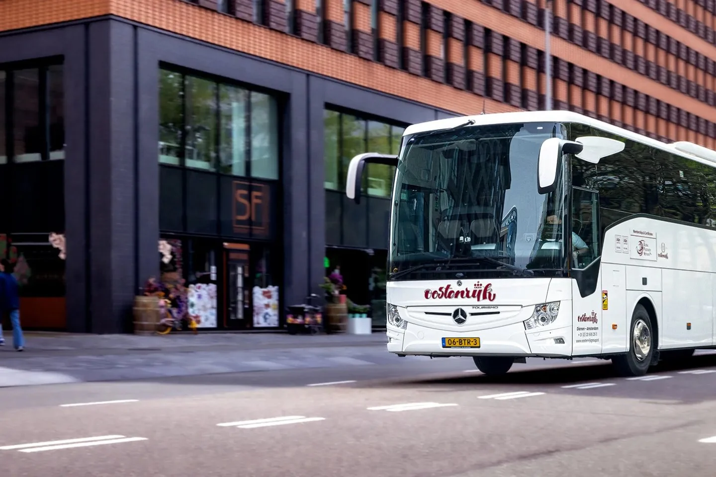 A white touring coach driving past a dark brick building