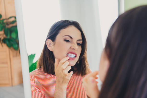 Young woman examining her teeth in mirror with a playful expression at home Charming young woman with bob haircut inspecting her teeth in the mirror. Her expression is playful and curious, embodying a casual and comfortable home atmosphere. checking teeth in mirror stock pictures, royalty-free photos & images