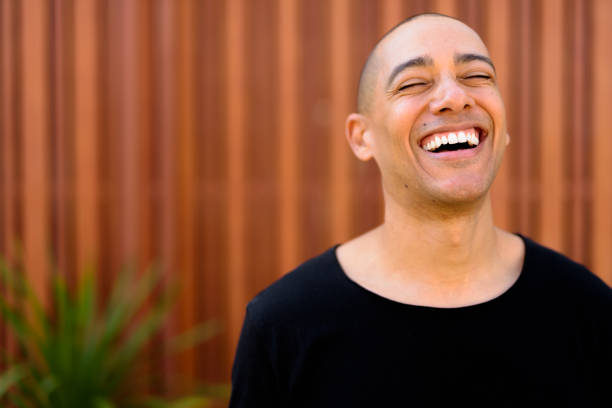 Portrait Of Handsome Bald Man Laughing Outdoors With Eyes Closed Portrait Of Handsome Bald Man Outdoors With Shallow Depth Of Field Candid, mid-shot of a late-30s man laughing naturally with teeth visible, outdoors in soft golden light stock pictures, royalty-free photos & images