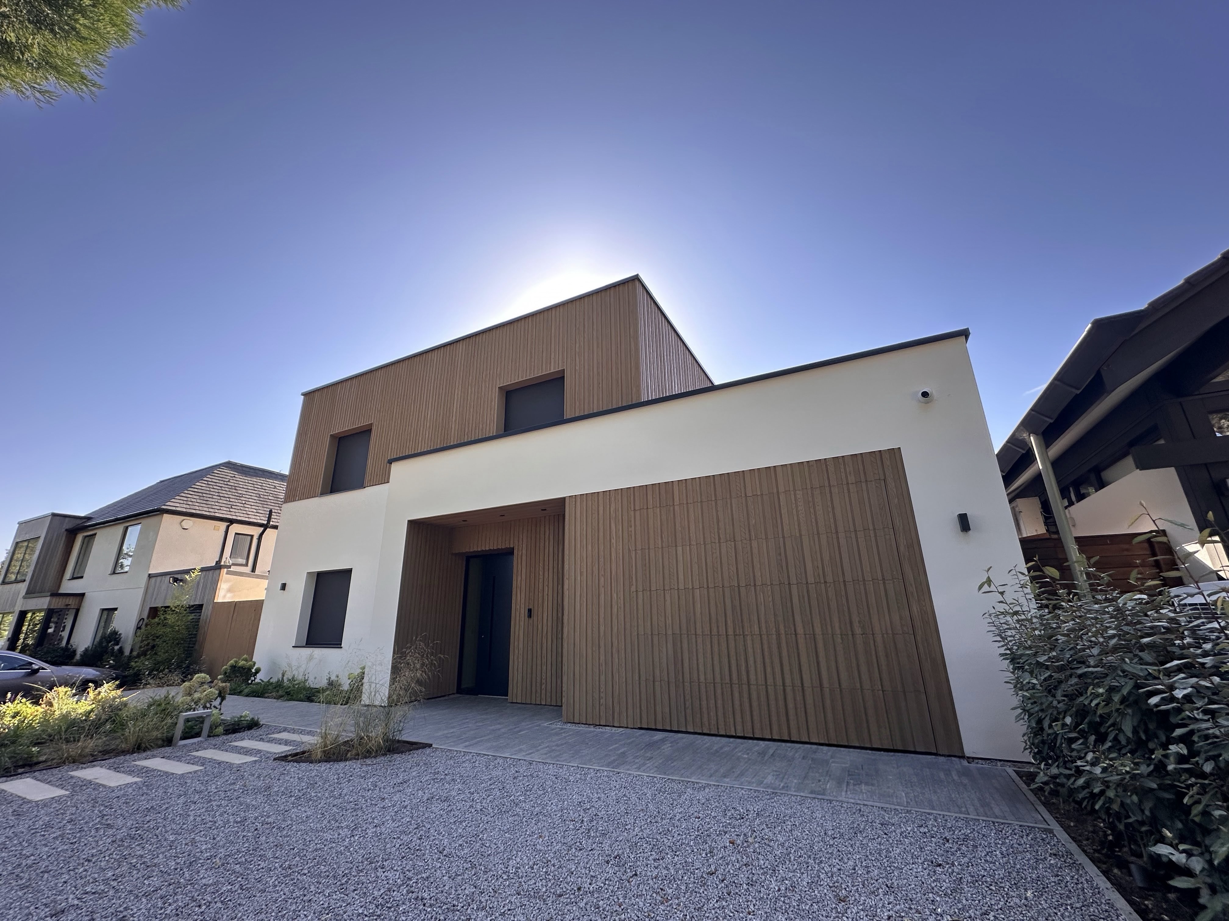 Energy-efficient net zero home with white cladding, large glass windows, and elevated structure, designed for sustainability and resilience.