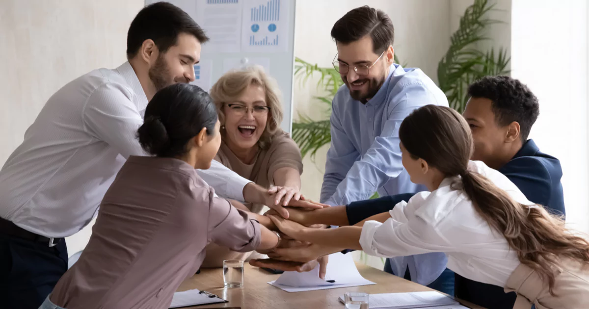 Groupe de collaborateurs souriants en fin de session d'escape game, certains levant les bras en signe de victoire, ambiance chaleureuse et détendue dans une salle lumineuse. Coffre ouvert sur la table, atmosphère de réussite collective.
